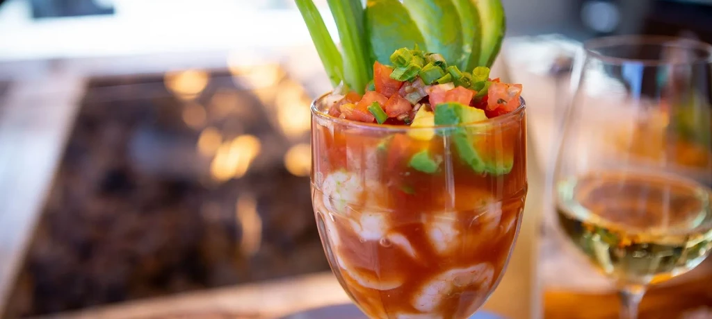 Shrimp cocktail with diced tomatoes, avocado, and a white wine glass.