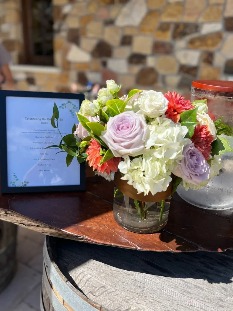 Flower bouquet and menu on a barrel-top table outdoors.