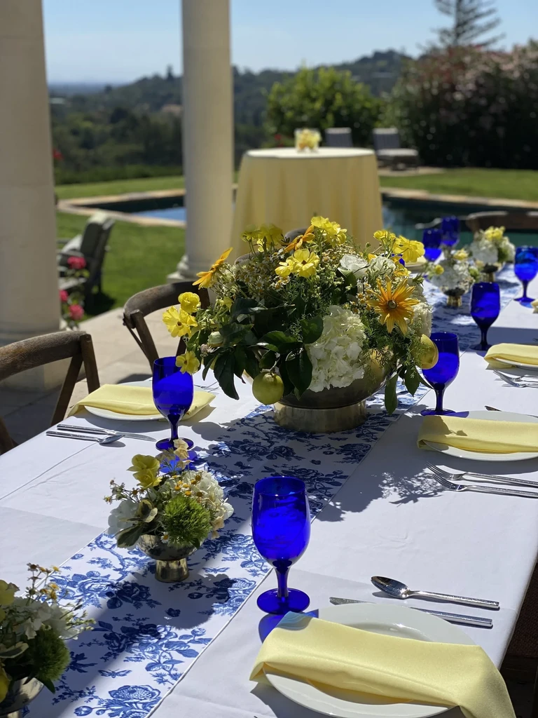 A set table on a patio overlooking a pool and green hills.