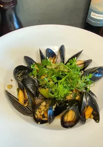 A white bowl filled with steamed mussels, garnished with greens.