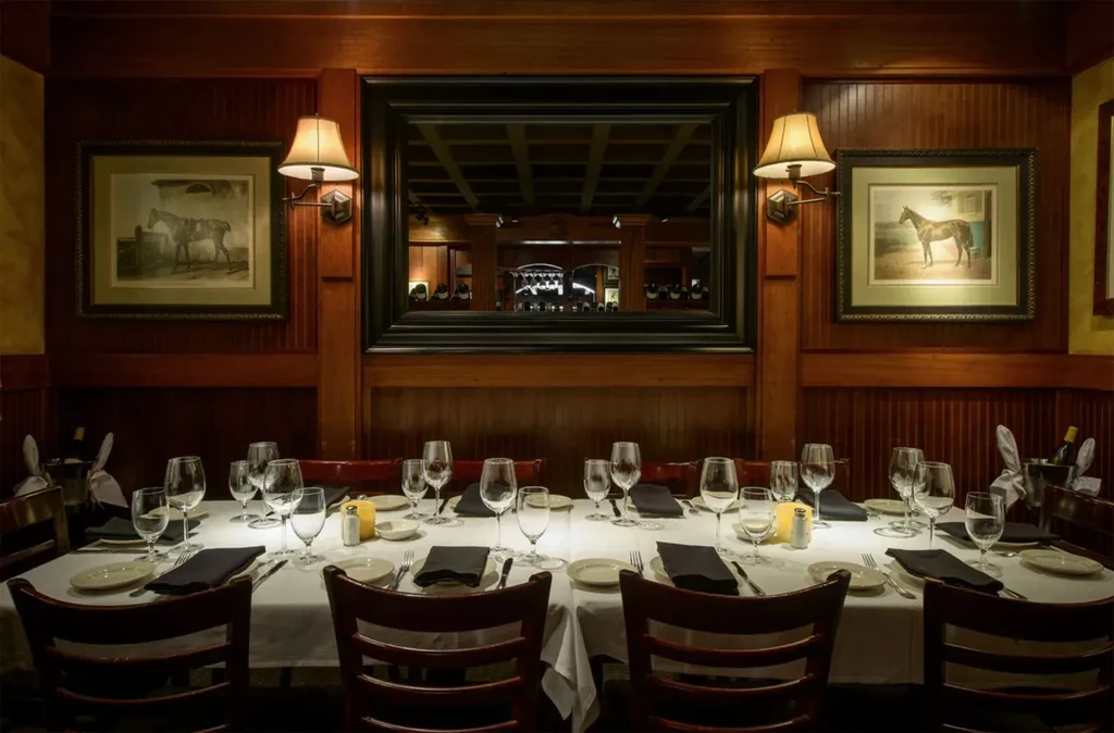 Elegantly set dining table in a wood-paneled room with horse paintings.