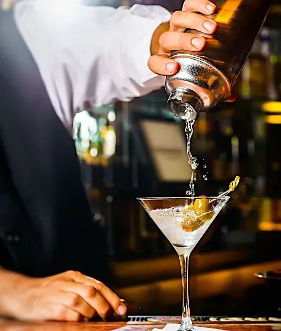 A bartender pours a martini from a shaker into a glass.