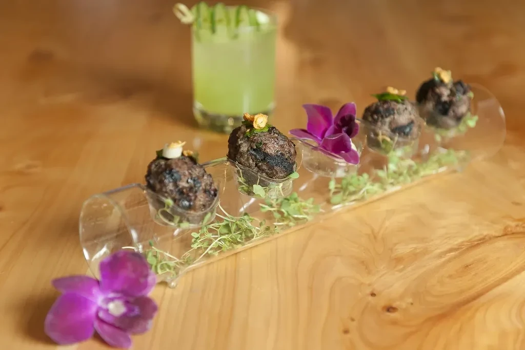Meatballs and microgreens on a clear tray with a green drink.