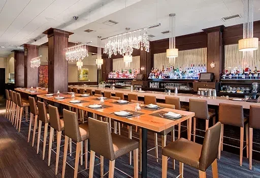 Long dining table and bar with rows of liquor bottles and hanging lights.