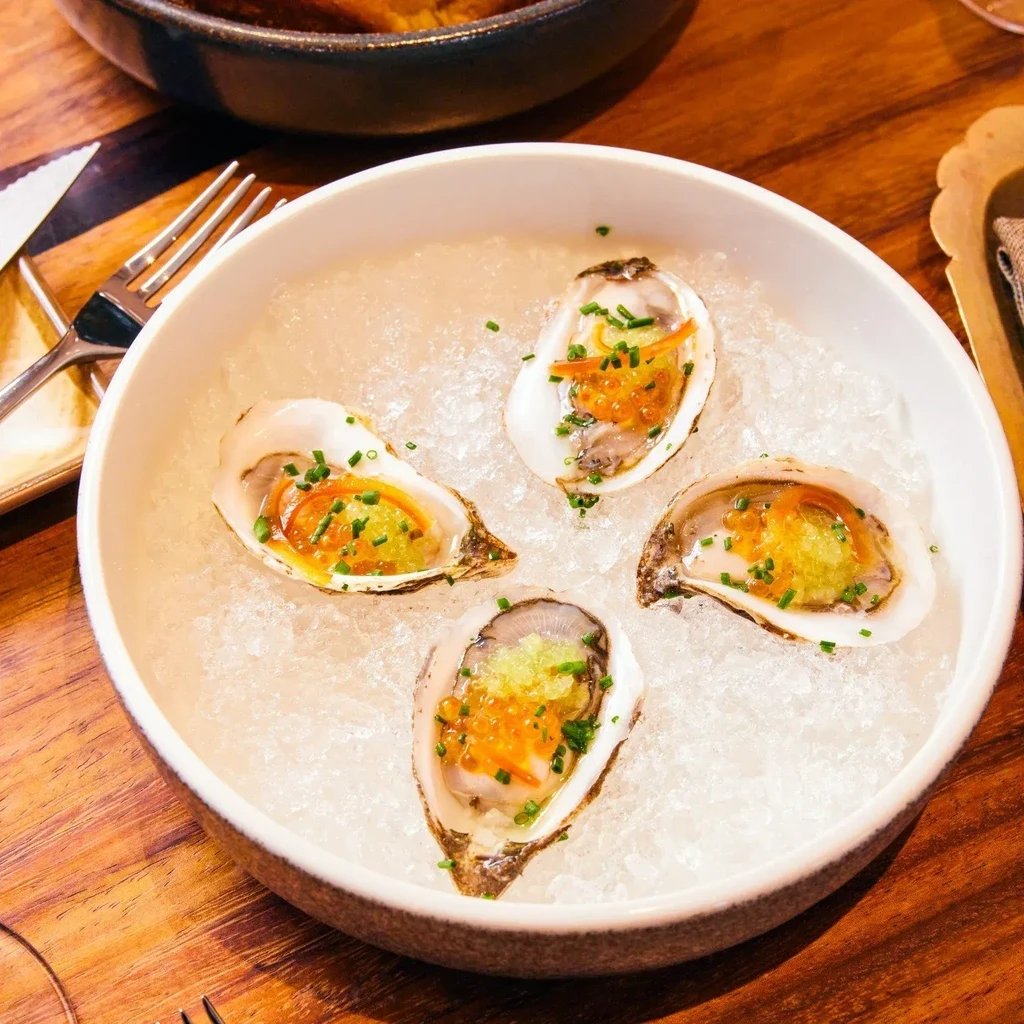 Four garnished oysters on ice in a white bowl.