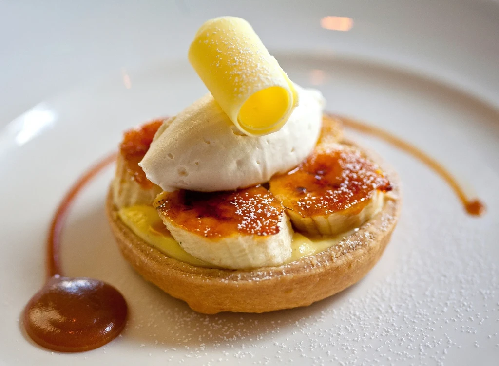 Banana tart with whipped cream, sugar curl, and caramel drizzle.