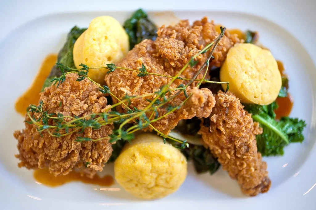 Fried chicken, biscuits, and greens on a white plate.