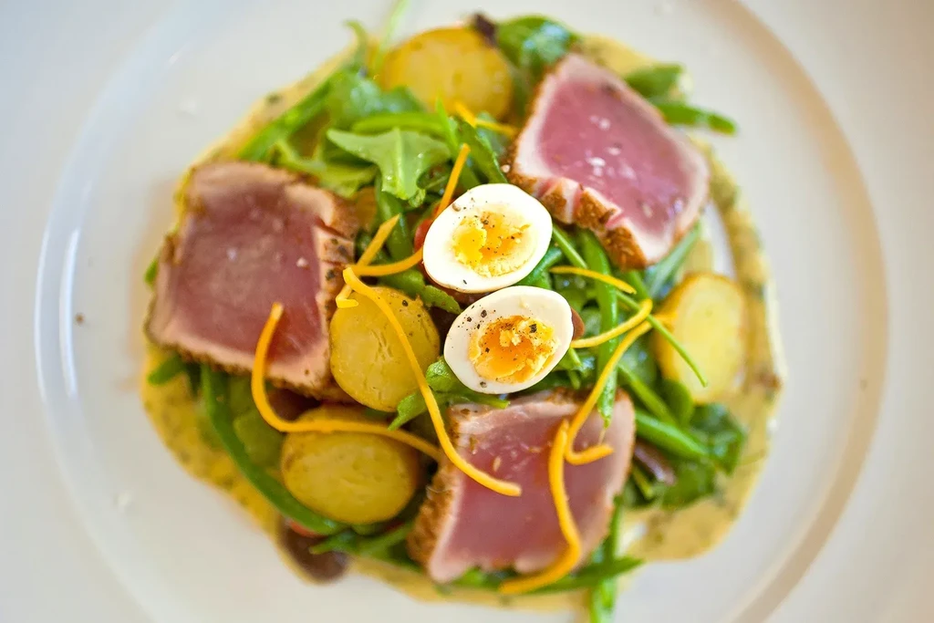 Seared tuna with green beans, potatoes, and hard-boiled eggs on a plate.