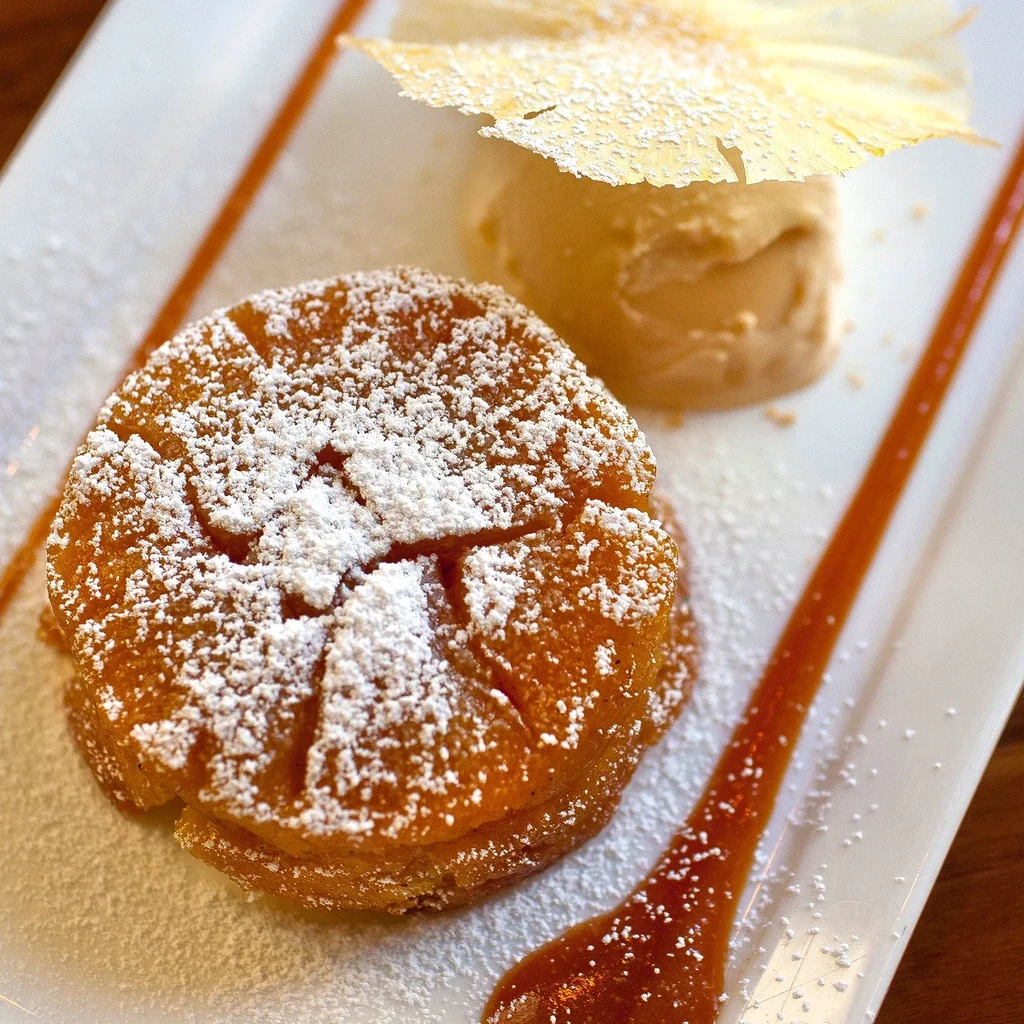 Tarte Tatin with vanilla ice cream and caramel drizzle on white plate.