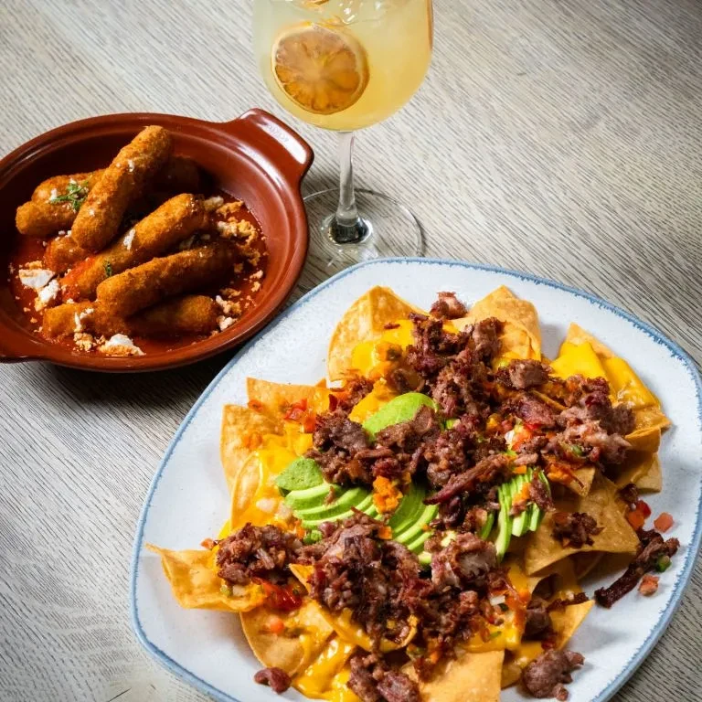 A plate of nachos with meat and avocado, and a bowl of fried food.