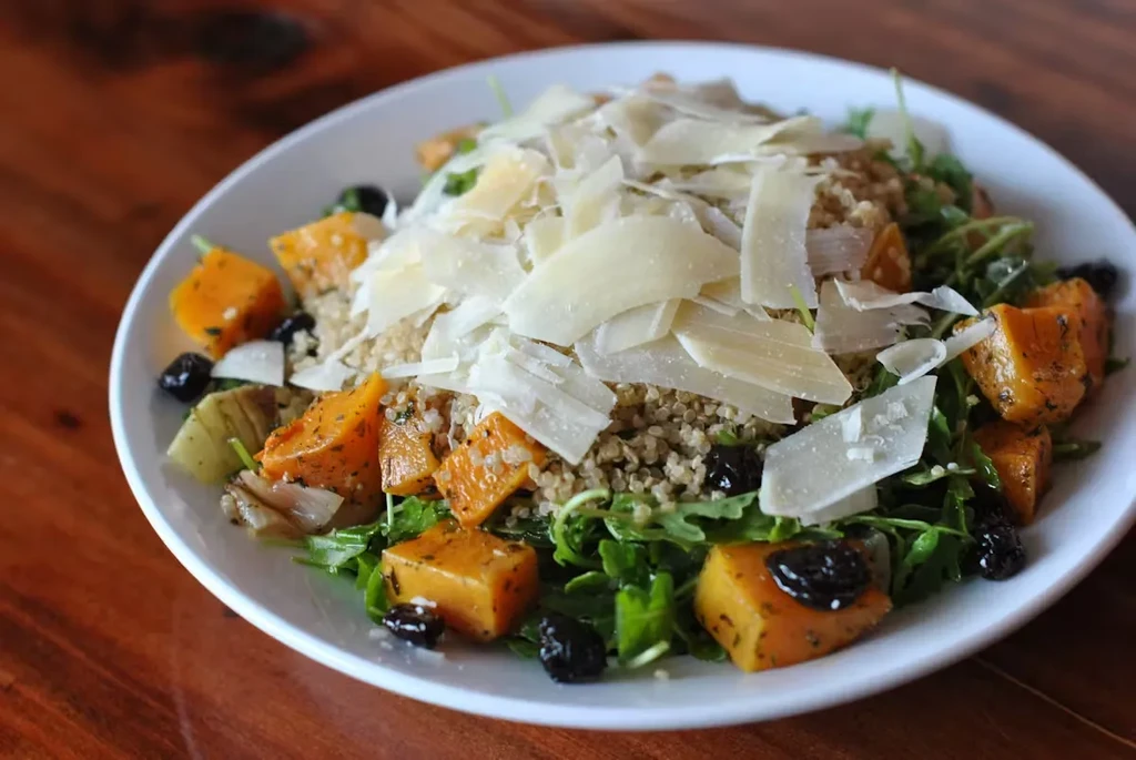 A butternut squash and quinoa salad with shaved Parmesan on a white plate.