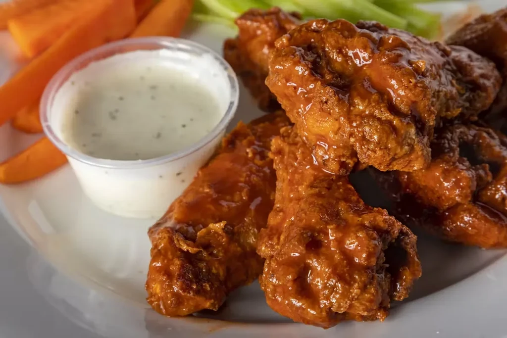 A plate of buffalo wings, ranch dressing, carrots, and celery.