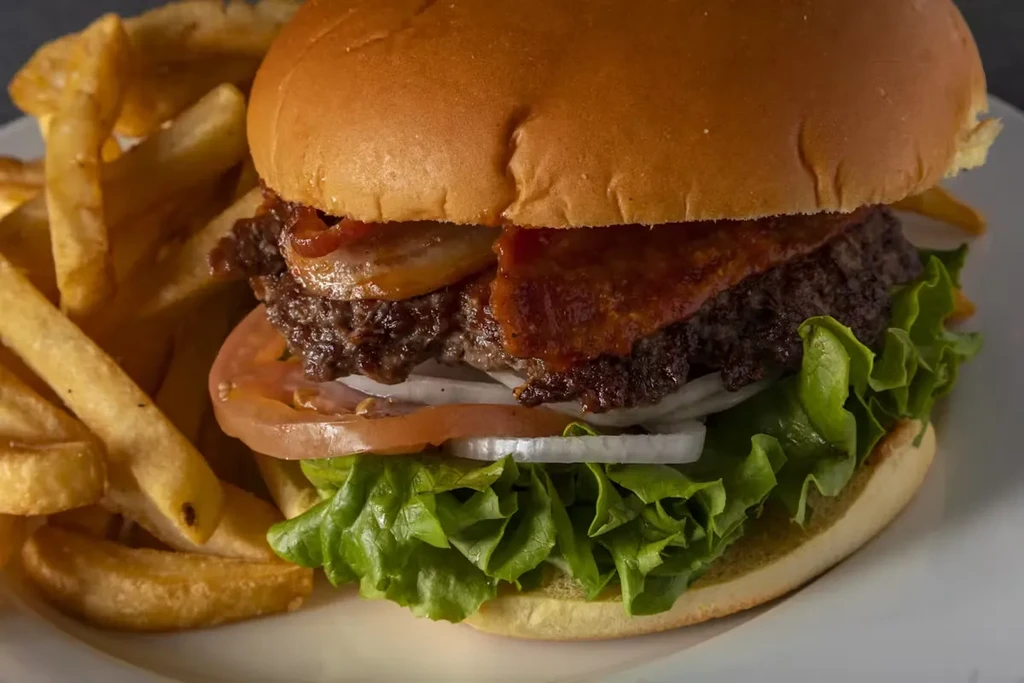 Close-up of a bacon cheeseburger with fries on a white plate.