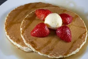 Two pancakes topped with strawberries, butter, and syrup on a plate.