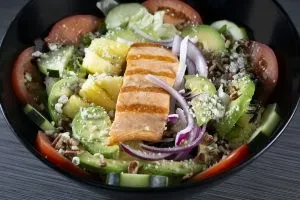 A grilled salmon fillet on a salad of tomatoes, cucumbers, avocado.