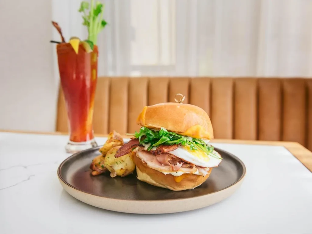 Breakfast sandwich with egg and bacon, side of potatoes and a Bloody Mary.
