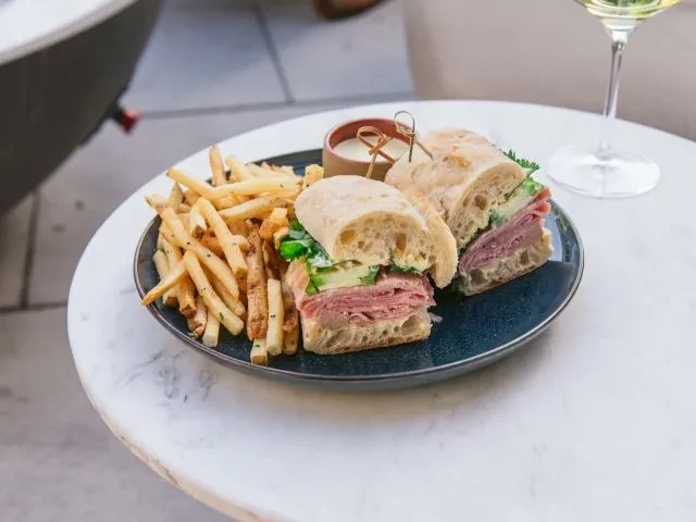 A ham sandwich cut in half, fries, and dip on a plate.