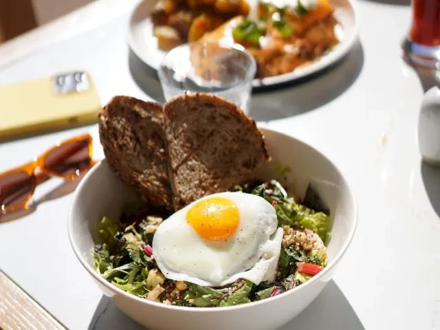 Breakfast bowl with egg and toast, sunglasses, and phone on a table.
