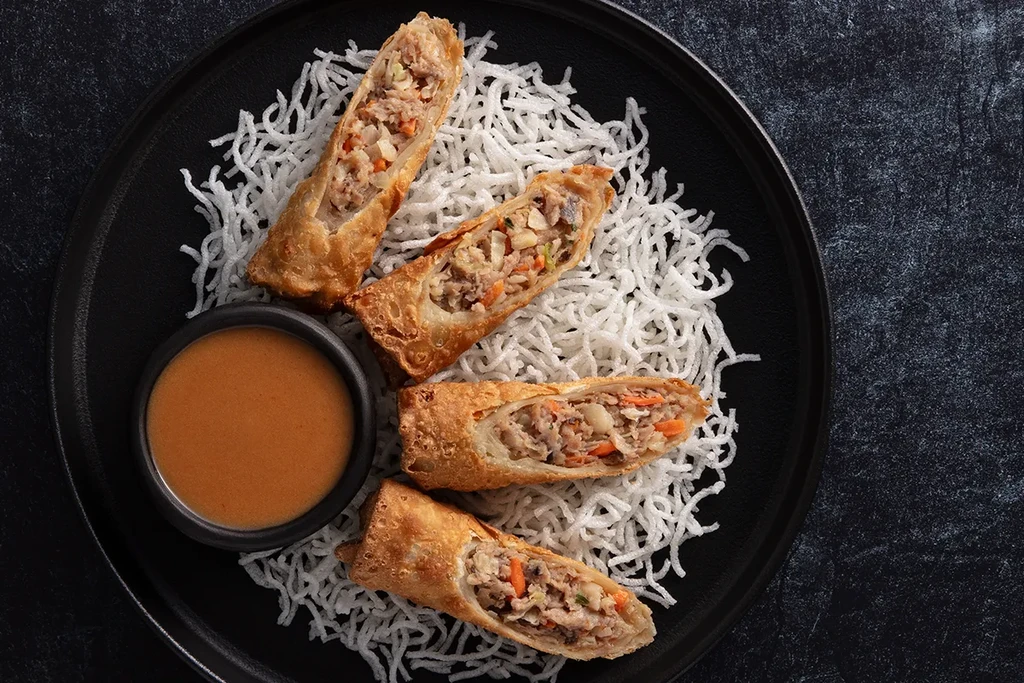 Four fried egg rolls, visible filling, served with dipping sauce.