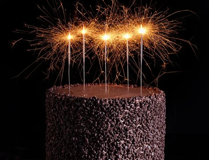 Chocolate cake with chips, glossy frosting, and five lit sparklers.