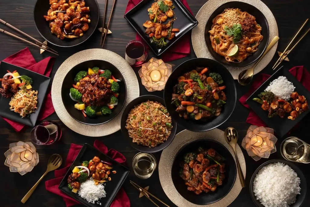 Elegant dark table with various Asian dishes and red wine.