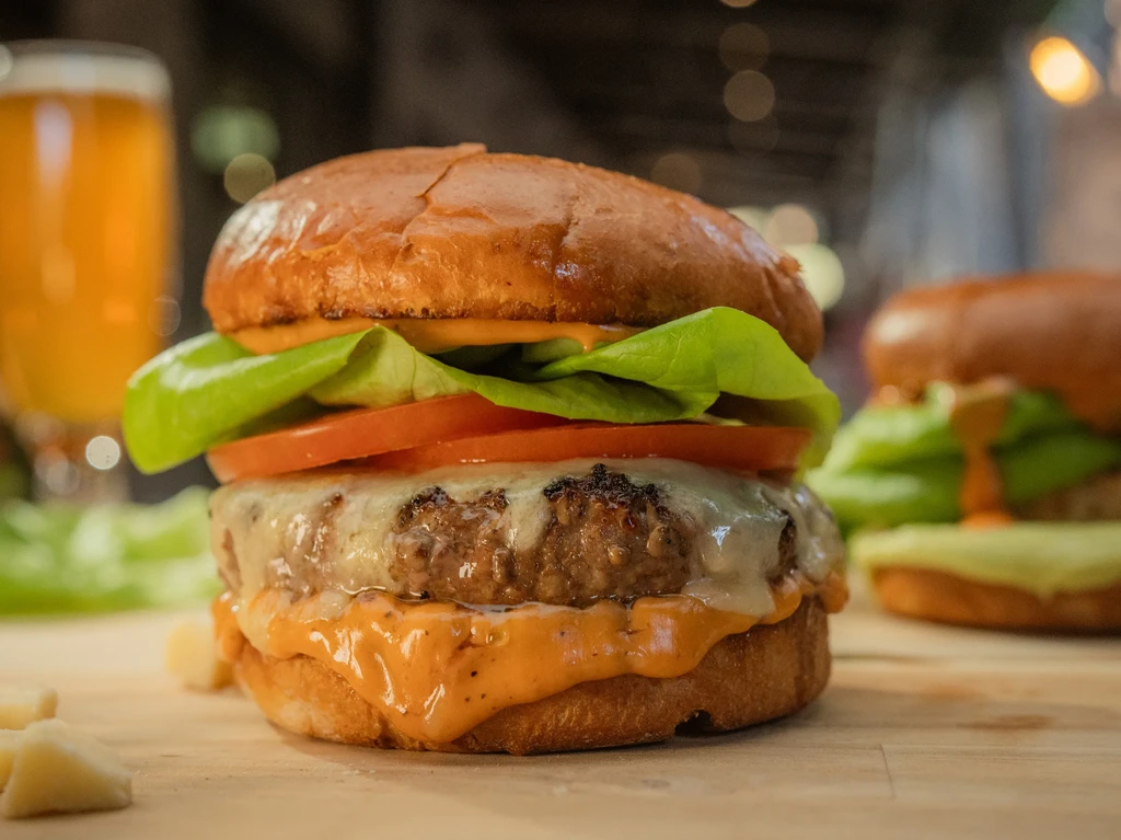 Two cheeseburgers with lettuce, tomato, and sauce, one in focus.