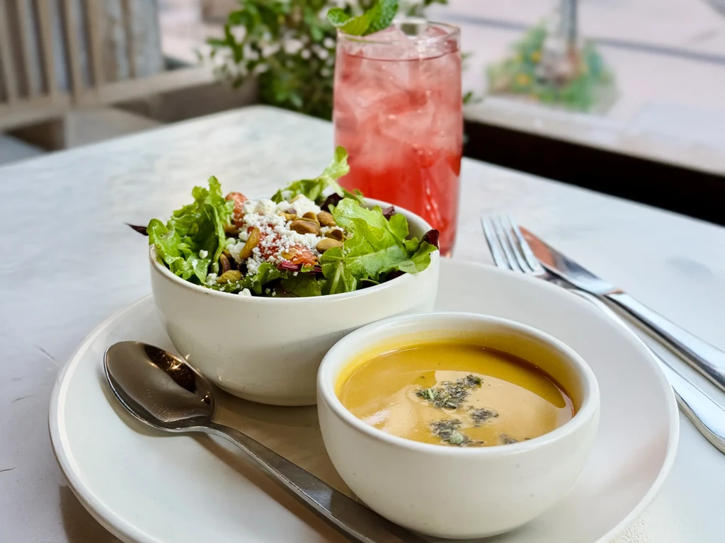 A bowl of salad, soup, and a red drink on a table.