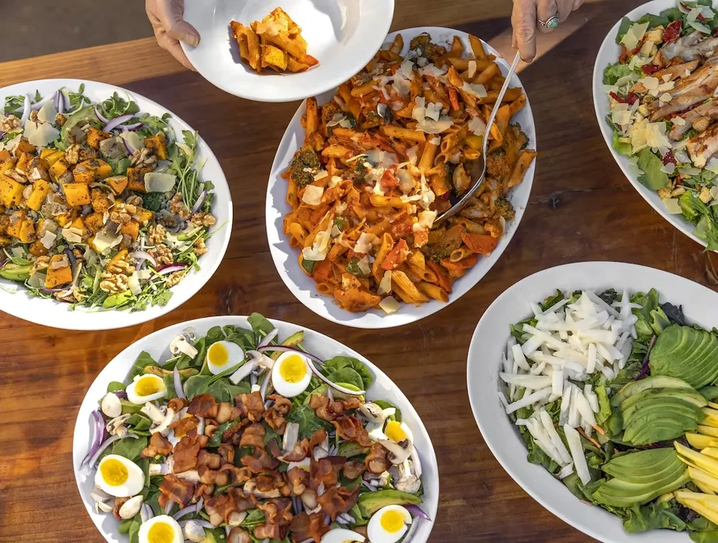 Overhead view of a feast with pasta and four plates of different salads.