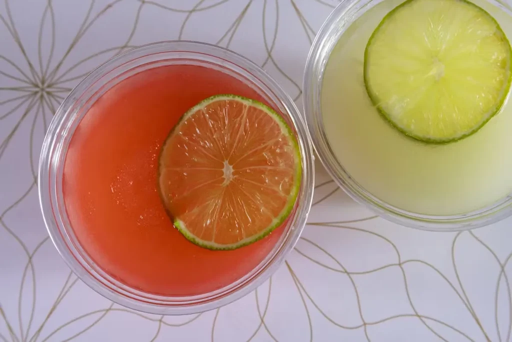 Overhead shot of two drinks with lime slices on a white patterned surface.