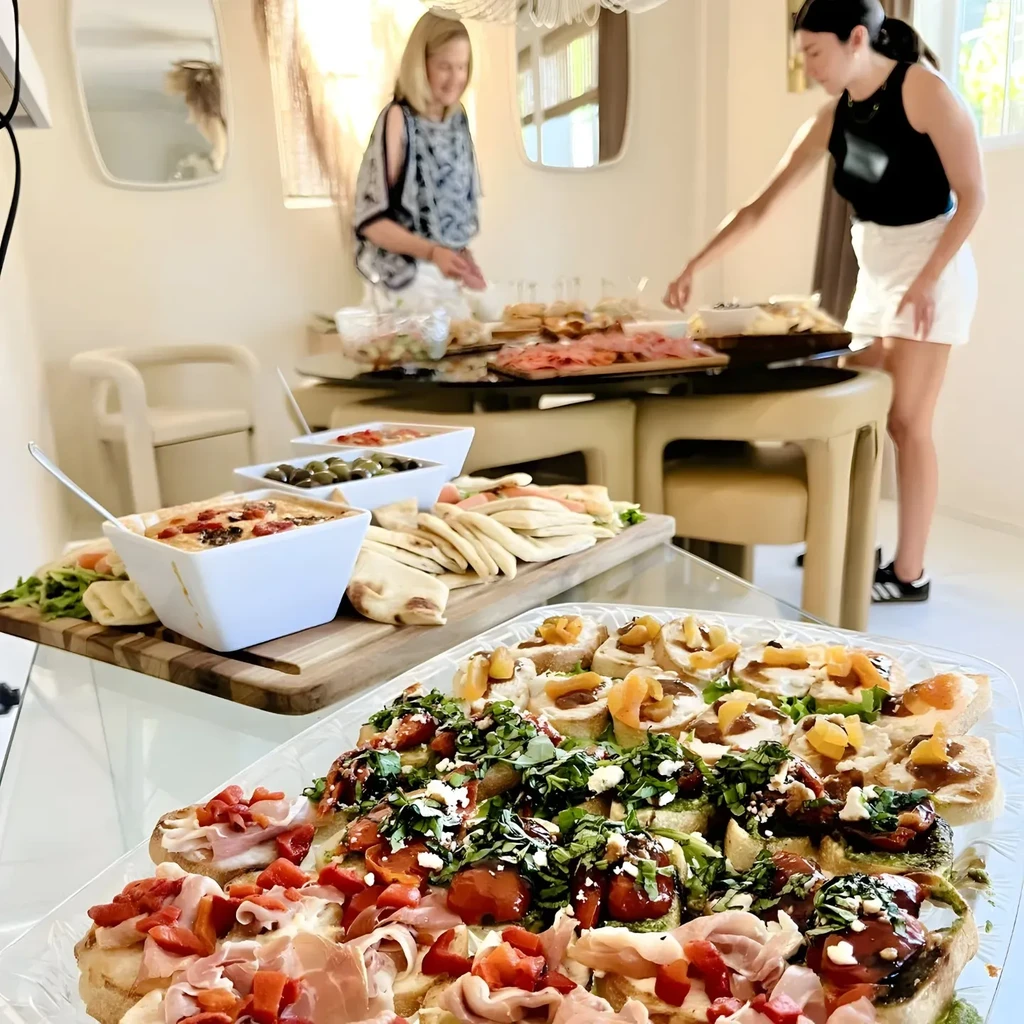 Two women arranging platters of food for a party.