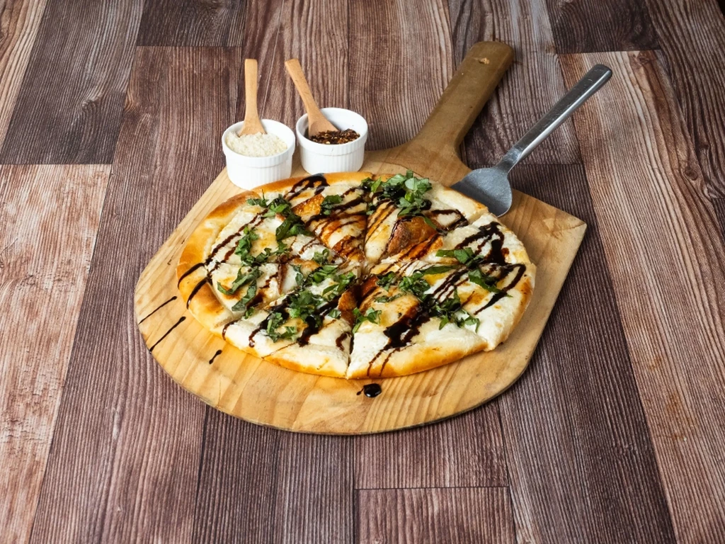 Pizza with balsamic glaze and basil on a wooden serving paddle.