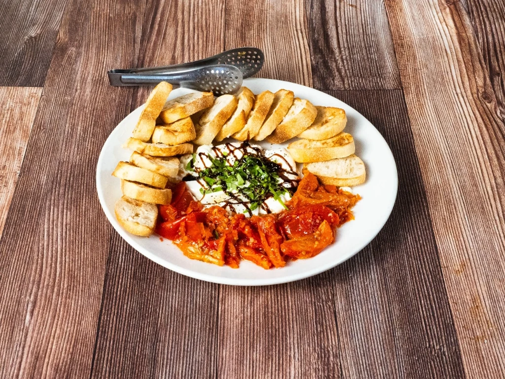 A white plate with burrata, toast, and roasted red peppers.