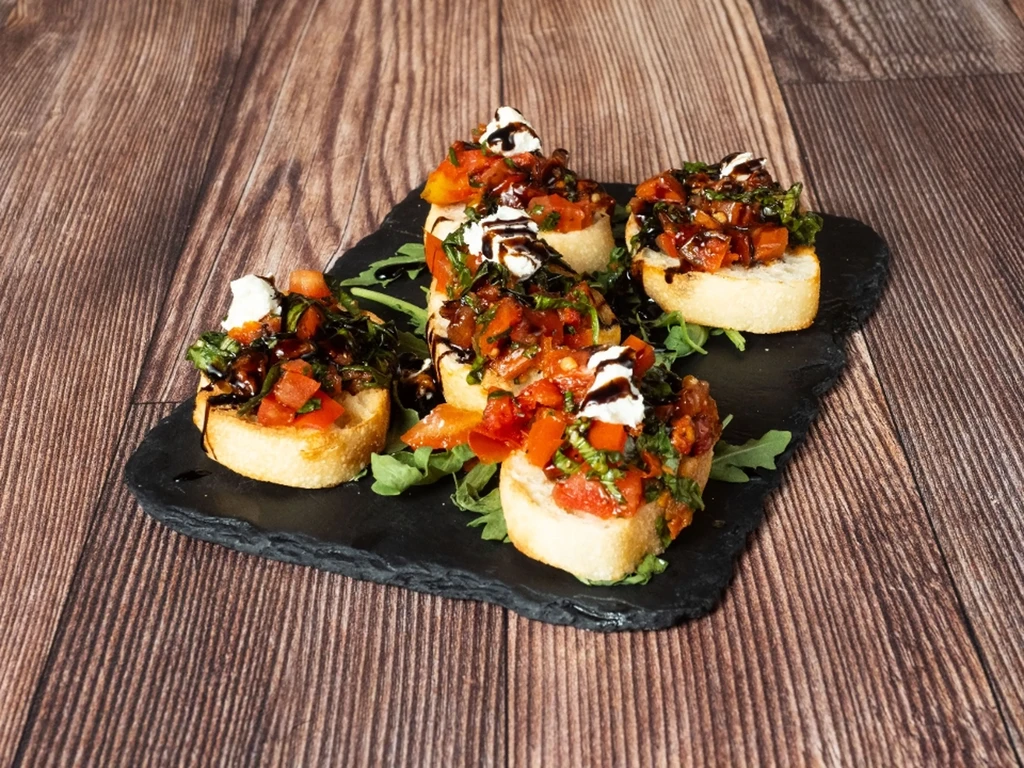Five pieces of bruschetta on a black slate against a wood background.