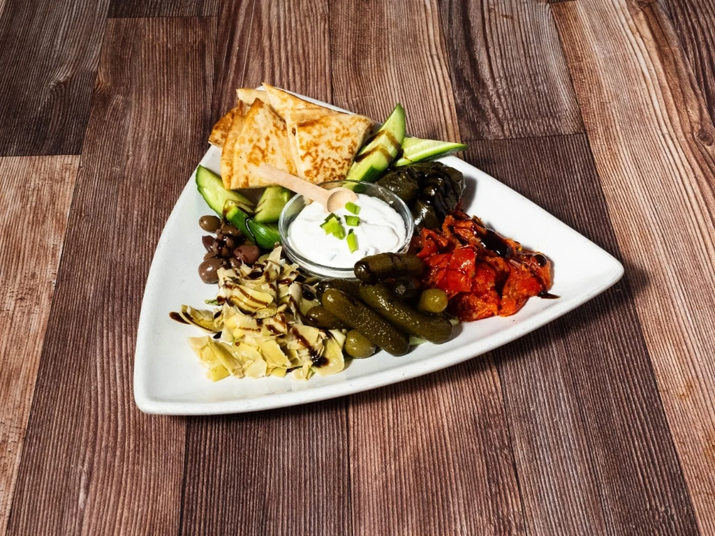 A triangular white plate on wood, filled with a Mediterranean appetizer platter.