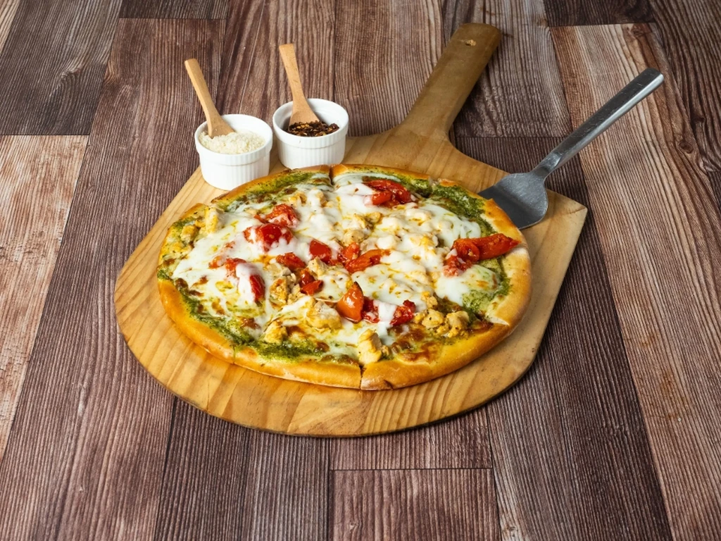 A round pizza on a wooden peel, with seasonings and a spatula.