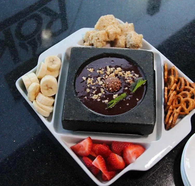 A white platter with various dipping snacks around a chocolate fondue.
