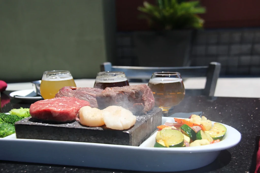 Steaming hot rock cooking with steak, scallops, and vegetables outdoors.