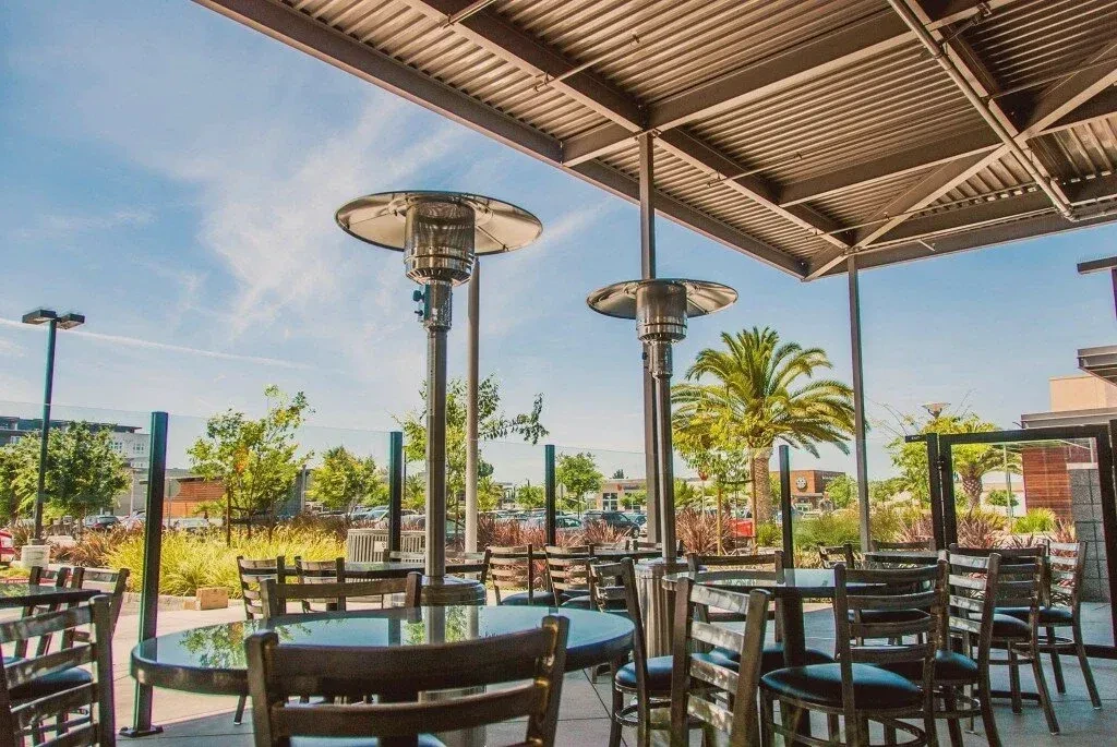 Outdoor patio dining with tables, chairs, two heaters, and palm trees.