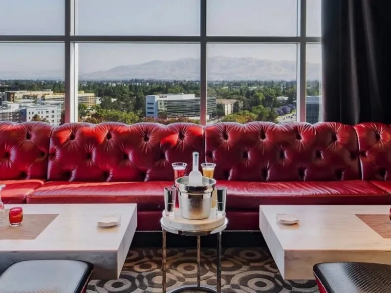 Red tufted leather couch with drinks overlooking a city and mountains.