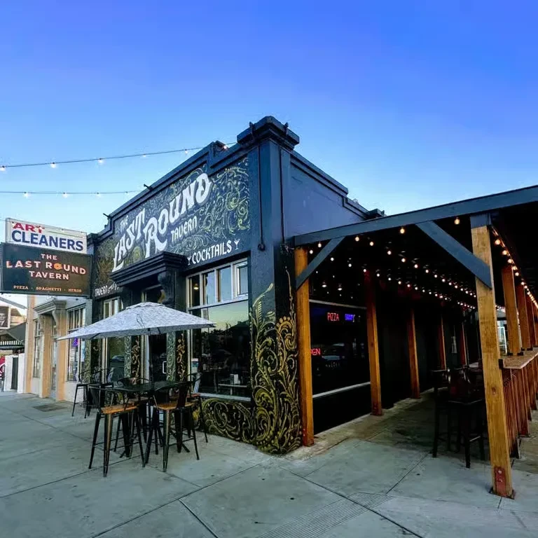 Dark Last Round Tavern exterior with ornate gold art, outdoor patio.