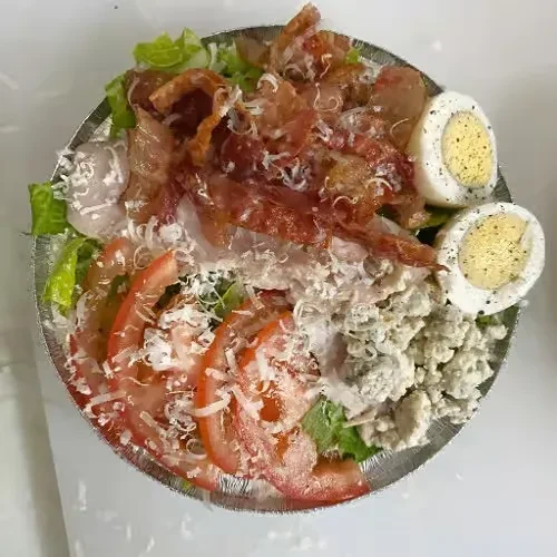 Salad in foil container: lettuce, tomato, cheeses, bacon, egg halves.