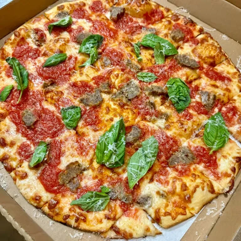 Round pizza in cardboard box with sausage, cheese, and basil.