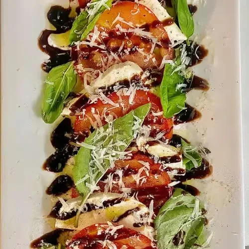 Layered Caprese salad with tomatoes, mozzarella, basil, balsamic, and grated cheese.