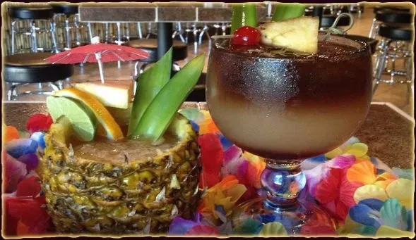Two tropical drinks, one in a pineapple, one in a glass.