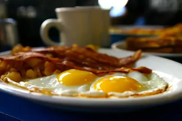 A plate with two fried eggs, bacon, and hash browns.