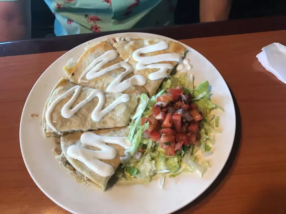 Quesadillas with sour cream, lettuce, and pico de gallo on a white plate.