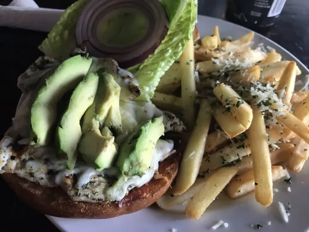 A grilled chicken sandwich with avocado, onion, lettuce, and a side of fries.