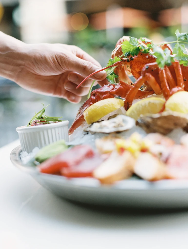 A hand garnishes a seafood platter with lobster, oysters, and fish.