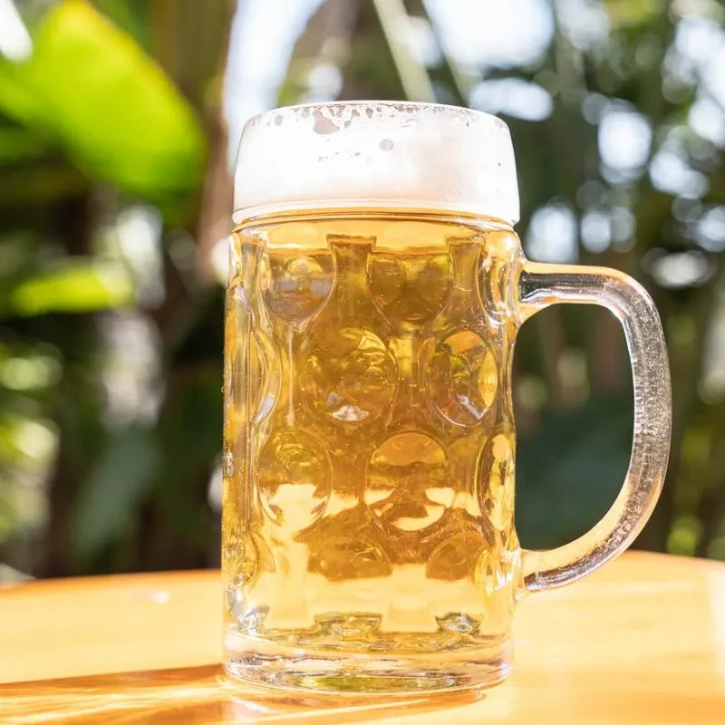 A glass beer mug with foam sits on a wooden table.