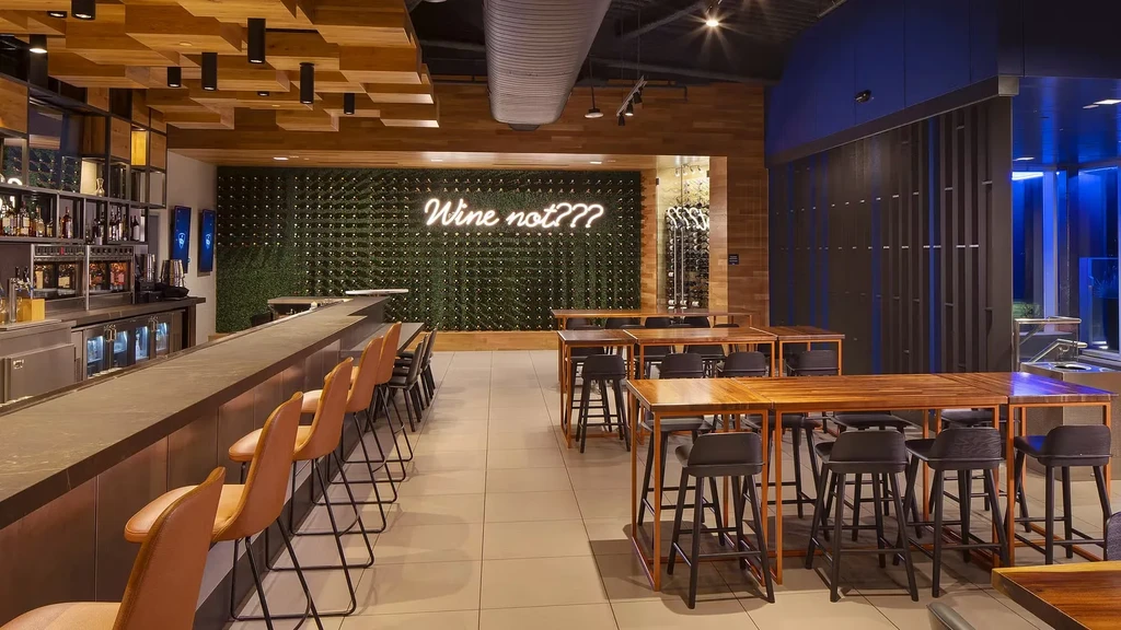 Modern restaurant bar with green foliage wall and "Wine not???" neon.
